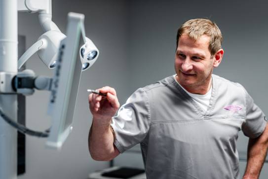 Zahnarzt betrachtet einen Monitor und bedient ihn mit einem Eingabestift, während er in einem Behandlungsraum steht.