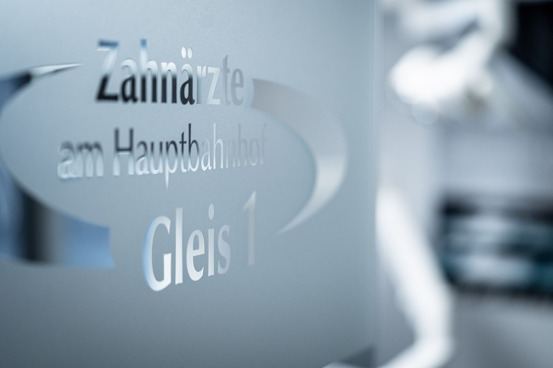 Milchglas-Tür mit der Aufschrift „Zahnärzte am Hauptbahnhof – Gleis 1“ in moderner Typografie.