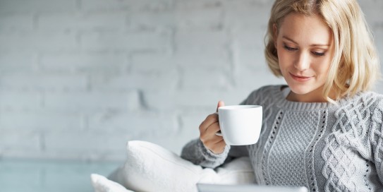 Frau schaut entspannt auf ihr Tablett und trinkt Kaffee