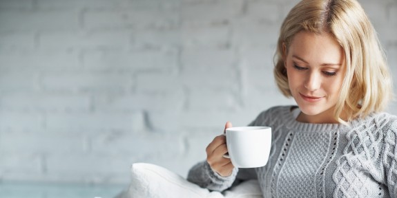 Frau schaut entspannt auf ihr Tablett und trinkt Kaffee