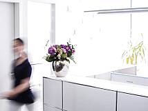 Heller Empfangsbereich einer Zahnarztpraxis mit Blumendekoration auf dem Tresen und unscharfer Bewegung einer vorbeigehenden Person.