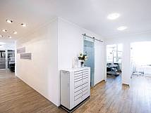 Heller Flur einer Zahnarztpraxis mit Holzfußboden, modernen Glastüren und Blick in zwei Behandlungsräume.